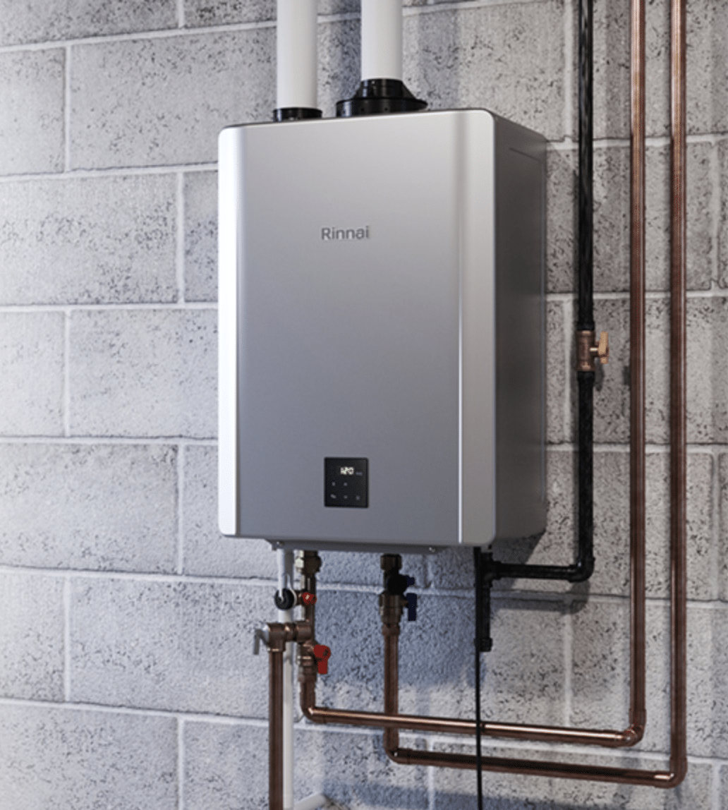 A wall-mounted Rinnai tankless water heater with digital display, connected to copper pipes, is installed on a gray cinder block wall.
