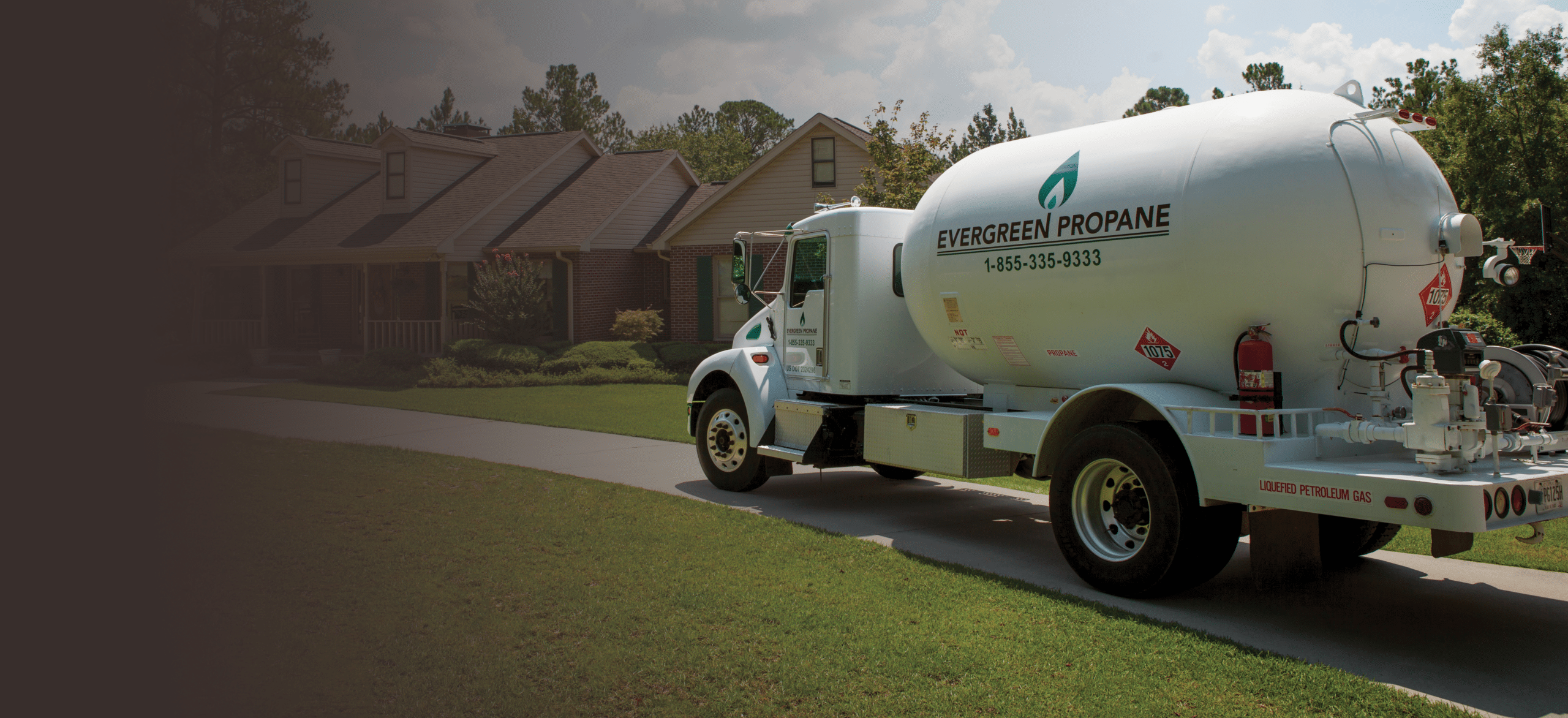 A white Evergreen Propane delivery truck is parked in the driveway of a suburban home, surrounded by a green lawn and trees under a sunny sky.